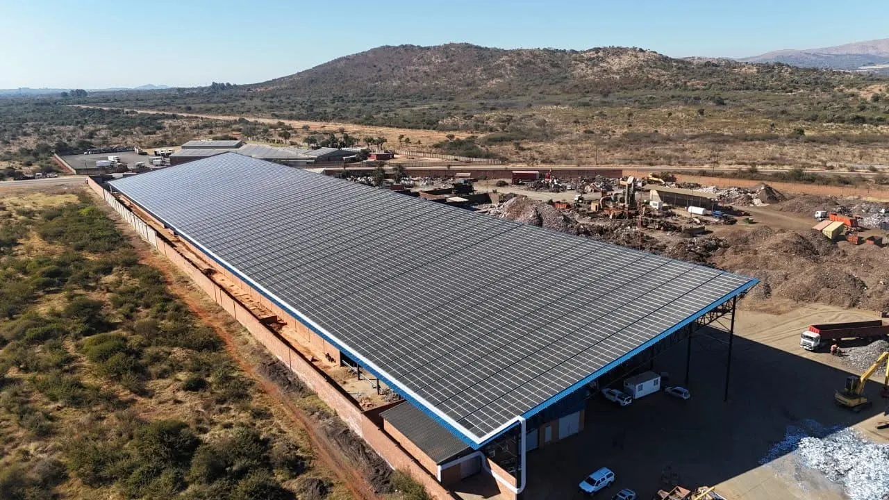 Aerial view of a completed solar array covering a long industrial shed roof in Hartbeespoort, beside a recycling yard