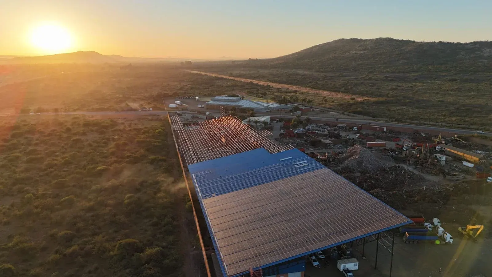 Aerial view at sunrise of an industrial shed roof in Hartbeespoort, partly covered in solar panels with roof trusses still open