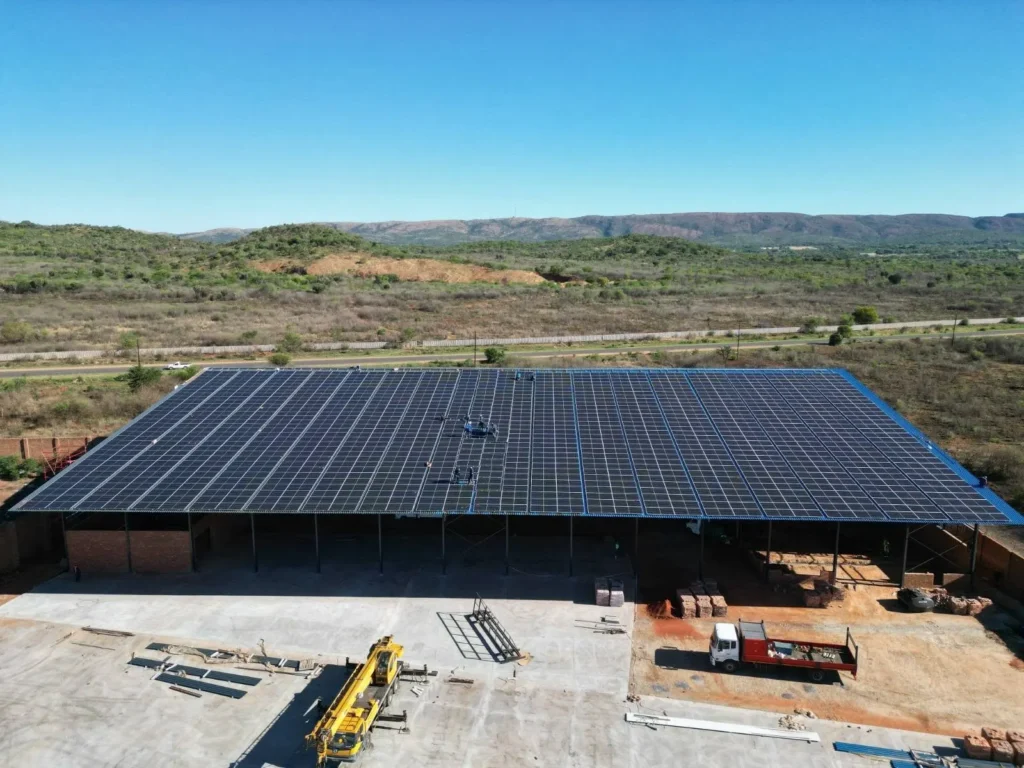 Aerial view of a Hartbeespoort steel shed roof completely covered in solar panels, with hills behind and a crane in the yard