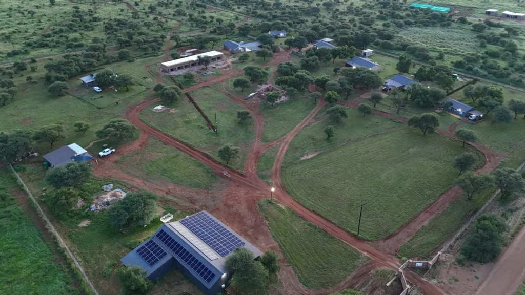 Aerial view at dusk of a rural property with solar panels on the roof of a large dark-roofed building in the foreground