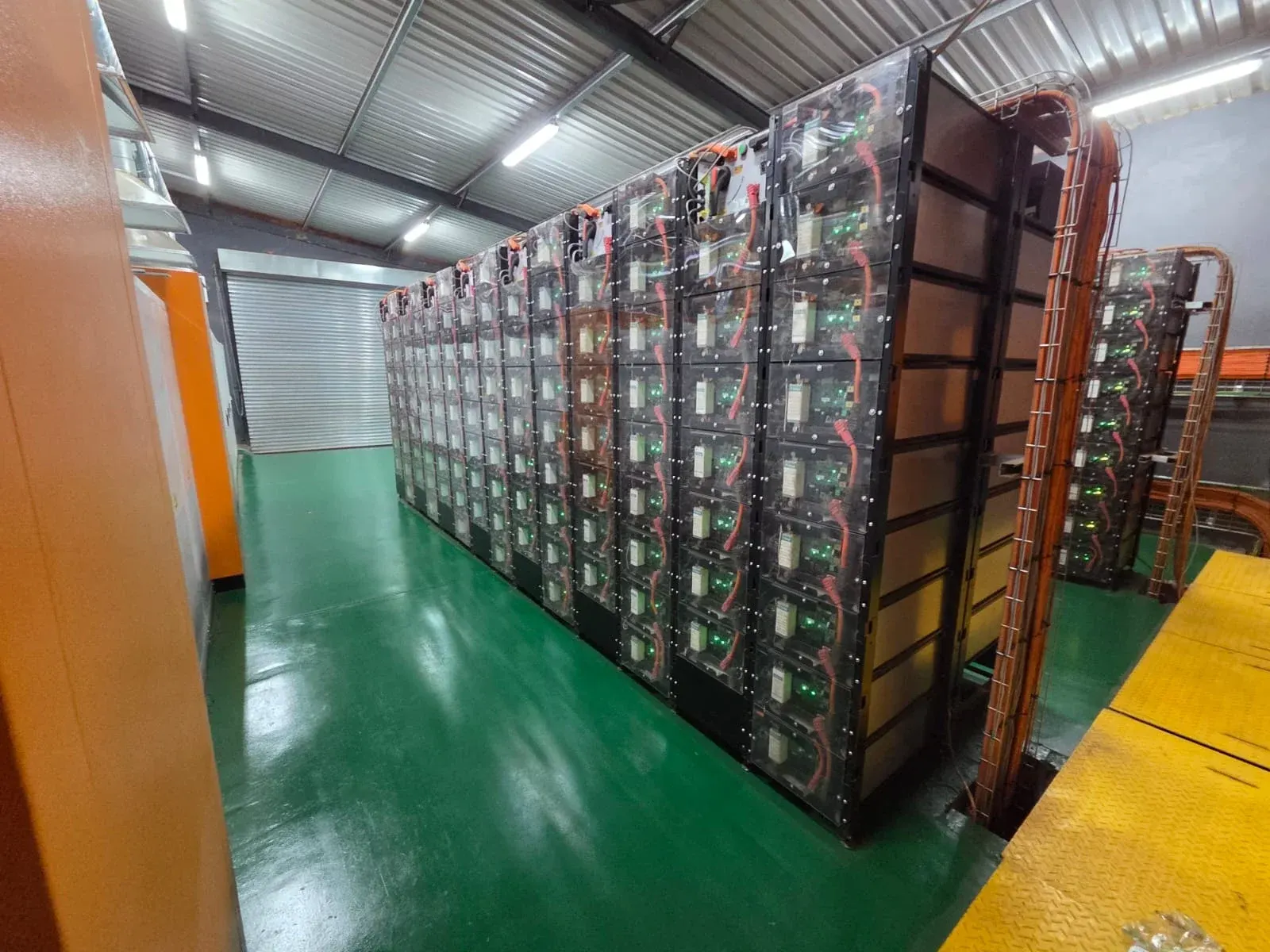 Large battery energy storage room with rows of stacked battery modules, orange cabling and a green epoxy floor