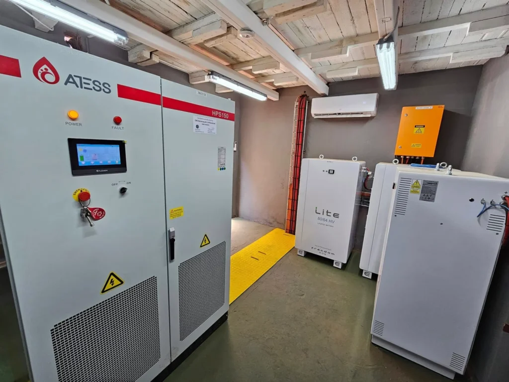 ATESS HPS150 hybrid inverter beside Freedom Won Lite HV lithium battery cabinets in a plant room with a timber ceiling