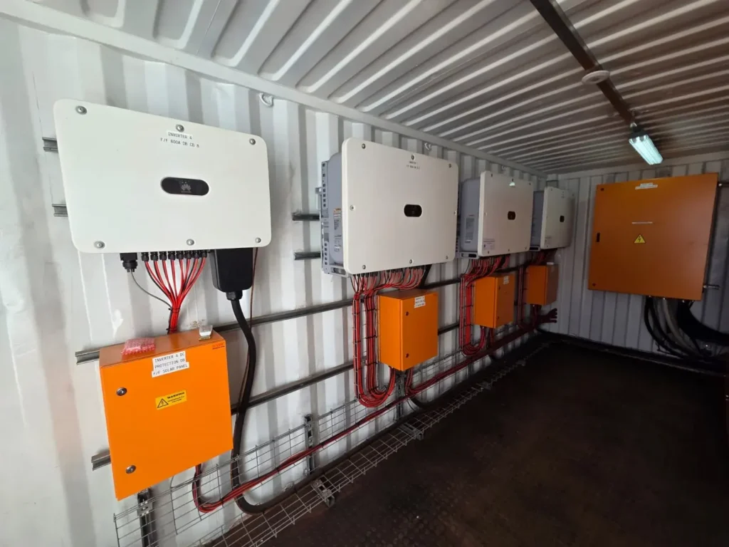 Four Huawei solar inverters on a container wall with orange DC protection boards and neatly bundled red and black cables